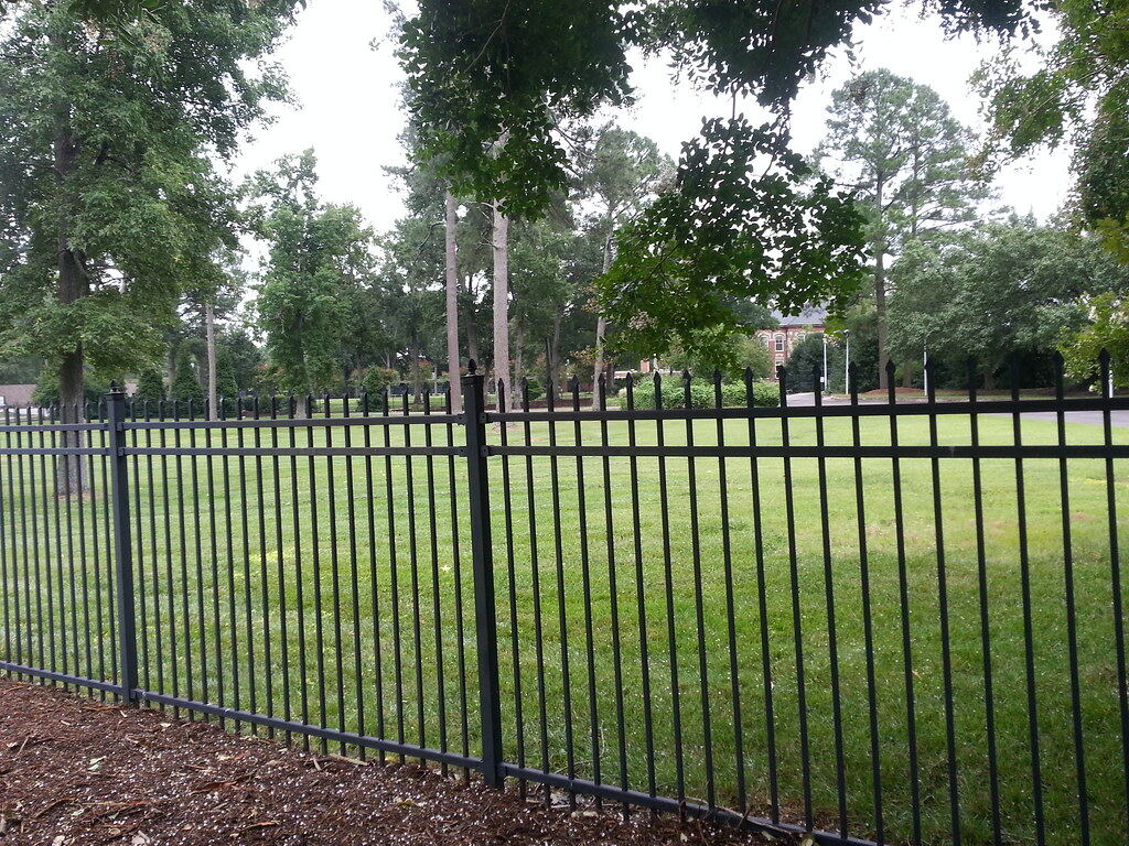 Black ornamental metal picket fence with spear-top finials along a lawn, shown as a style example of ornamental iron fencing