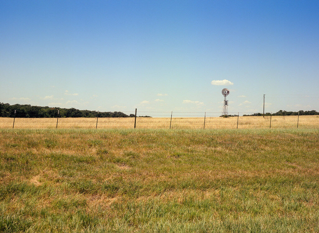 T-post and wire ranch fencing running across North Texas pastureland with a windmill in the distance, shown as a style example of ranch fencing